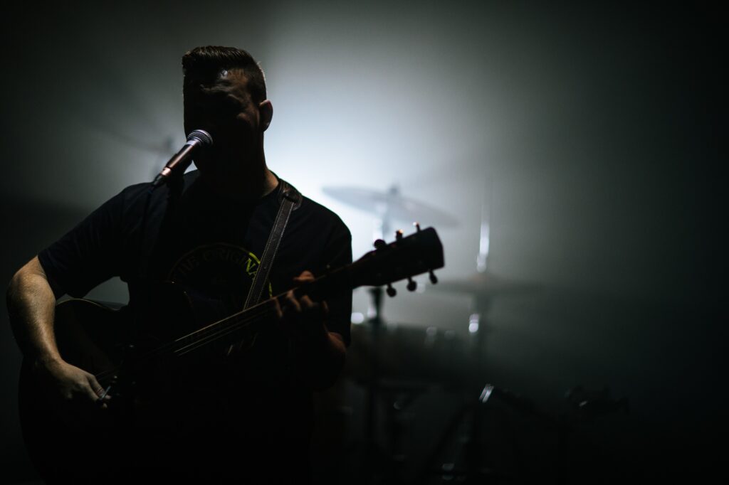 Guy singing in a worship band at church with his guitar